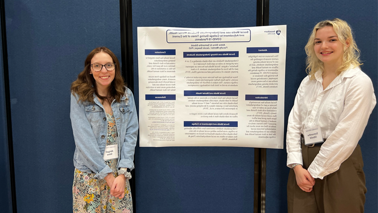 Female students standing by a poster displayed on a wall. 